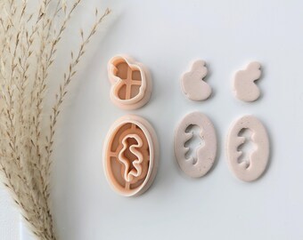 May include: A collection of light peach-colored polymer clay cutters in various shapes. The set includes two oval cutters with a tree-like design, two small abstract shapes, and two cutters with a cross and a curvy design.
