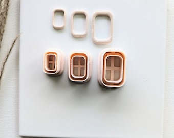 May include: Set of five plastic cookie cutters in the shape of windows. The cutters are in various sizes and have a light pink colour.