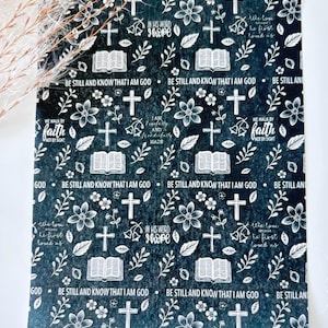 May include: A black sheet with a repeating white pattern featuring open books, crosses, flowers, and leaves. The text includes phrases such as Be still and know that I am God, In his word I hope, We walk by faith not by sight, and We love because he first loved us.