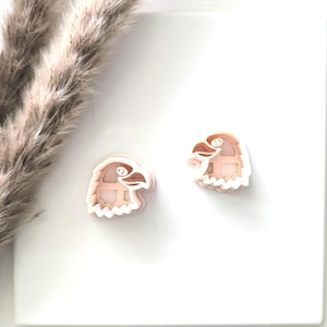 May include: A pair of peach-coloured eagle head earrings with white outlines. The earrings are layered and have a 3D effect.