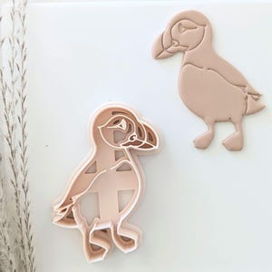 May include: Two brown plastic cookie cutters shaped like puffins. The puffins are standing upright with their wings outstretched.