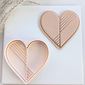 May include: A light pink heart-shaped cookie cutter with a geometric design. The cutter is made of plastic and has a smooth finish.