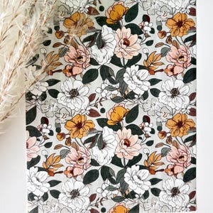 May include: A floral pattern featuring a variety of flowers in shades of white, peach, and gold, set against a light gray background. The design includes dark green leaves and stems, creating a botanical theme. The overall aesthetic is soft and inviting.