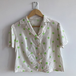 Può includere: Una camicia bianca a maniche corte con bottoni e pois verdi.