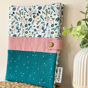 Peut inclure: Une housse de livre en tissu bleu turquoise avec des pois blancs et une bande en tissu rose. Le haut de la housse est blanc avec un motif floral et le texte "les petits panfaits" est dans le coin inférieur droit.