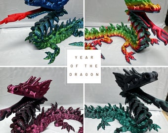 May include: Four 3D printed dragon figurines in different colors: blue, green, red, and black. Each dragon has a skeletal design and is posed in a dynamic, upright position. The text "YEAR OF THE DRAGON" is displayed in the center of the image.