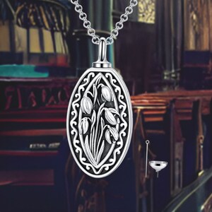 May include: Silver pendant necklace with an oval-shaped charm featuring an intricate design of snowdrop flowers. The charm has a detailed floral pattern and a delicate chain.
