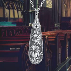 May include: A silver pendant necklace featuring an intricate design of a bee on a flower. The pendant is teardrop-shaped and hangs from a fine chain.