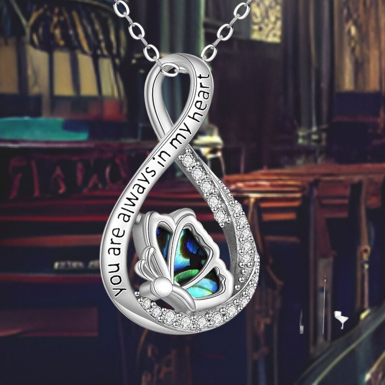 May include: Silver infinity necklace with a butterfly charm and the inscription "You are always in my heart".