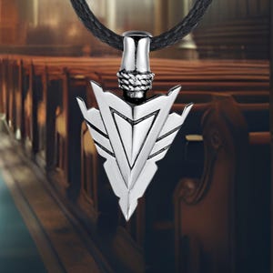 May include: A silver arrowhead pendant necklace with a black cord. The pendant is detailed with intricate lines and a pointed tip.