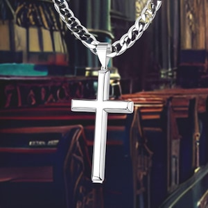 May include: A silver chain necklace with a large silver cross pendant. The cross is simple and has a slightly rounded shape.