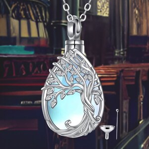 May include: Silver pendant necklace with a tree of life design. The pendant is a teardrop shape with a clear blue stone inside. The necklace comes with a small funnel and a tool for filling the pendant.