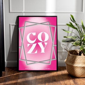 May include: A pink poster with the word "COZY" in white letters inside a silver frame. The poster has the text "This is a reminder she's a goddess she's a hero" at the top and bottom.