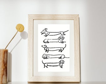 Op de afbeelding: Een zwart-witte lijntekening van vijf teckels in een ingelijste print. De teckels zijn in verschillende posities getekend, sommige liggen, sommige staan en sommige rennen. De print is ingelijst in een licht houten lijst.