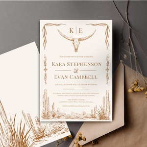 May include: A wedding invitation with a southwestern theme. The invitation features a stylized drawing of a desert landscape with cacti and a bull skull. The text reads "KE Together with their families Kara Stephenson & Evan Campbell Joyfully invite you to their wedding Saturday, the twenty-eighth of June, two thousand twenty-five at five o'clock in the evening The Perfect Venue 60 Perfect Venue Way, Atlanta, GA 30308 www.yourweddingwebsite.com"