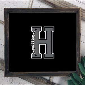 May include: Framed black sign with a gray letter "H" outlined in white. A football graphic is on the left side of the letter. The sign is in a dark brown wooden frame.