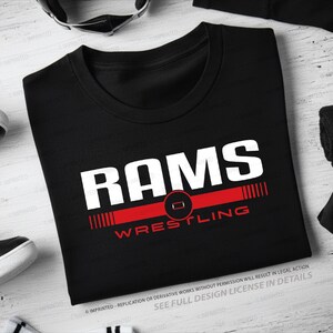 May include: Black crew neck t-shirt with the word "RAMS" in large white letters above a red stripe with the word "WRESTLING" in red. The shirt is surrounded by athletic gear.