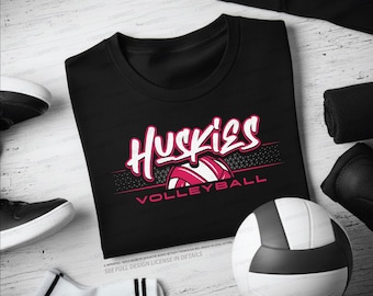 May include: Black t-shirt with the word "Huskies" in white and pink script, with a volleyball graphic. The word "Volleyball" is below the graphic in pink. A volleyball and athletic gear are in the background.