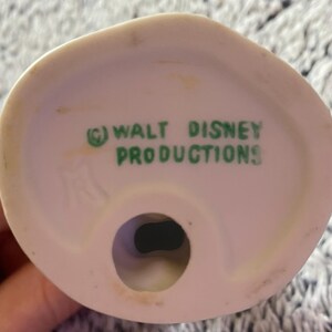 May include: A close-up of the bottom of a white ceramic figurine. The text "(C) WALT DISNEY PRODUCTIONS" is printed in green. The figurine has a circular hole at the base.