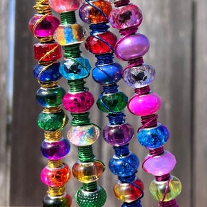 May include: Four colorful beaded keychains with different colored beads and wire wraps. The keychains are hanging from black metal hooks.