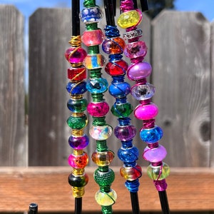 May include: Five black metal hooks with colorful beaded accents. The beads are various shapes and sizes and are strung on wire. The hooks are hanging from a metal bar.