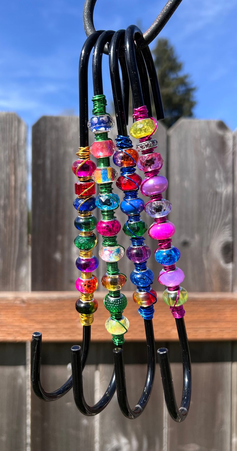 May include: Five black metal hooks with colorful beaded accents. The beads are various shapes and sizes and are strung on wire. The hooks are hanging from a metal bar.