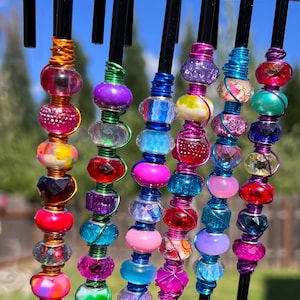 May include: A set of seven colorful beaded hooks, each with a different combination of beads in shades of pink, blue, green, purple, and red. The hooks are made of black metal and are wrapped with wire.
