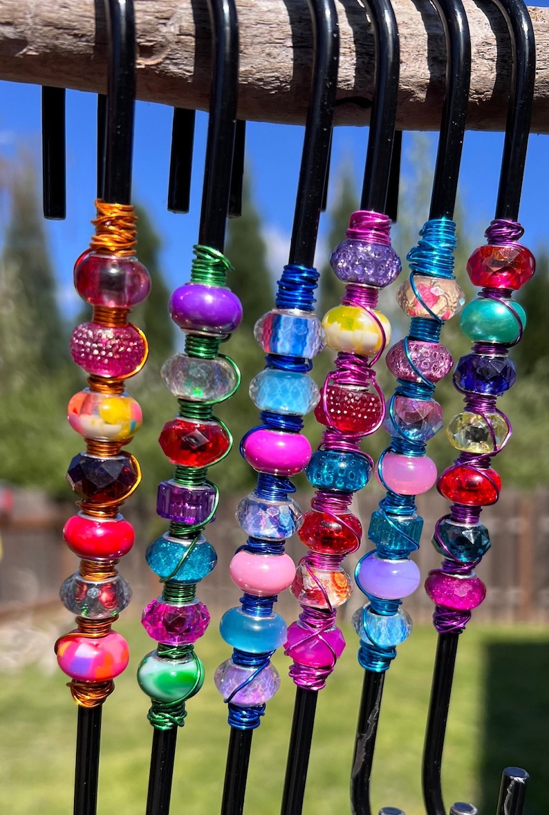 May include: A set of seven colorful beaded hooks, each with a different combination of beads in shades of pink, blue, green, purple, and red. The hooks are made of black metal and are wrapped with wire.