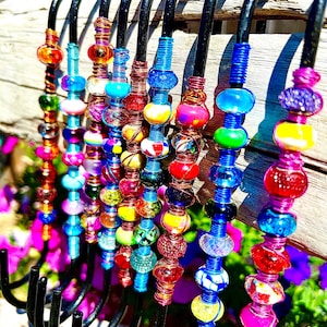May include: A set of 10 colorful beaded hooks, each with a different pattern of beads. The hooks are made of black metal and are designed to hang on a wall or door. The beads are made of glass and are in various colors, including red, blue, green, yellow, and purple.
