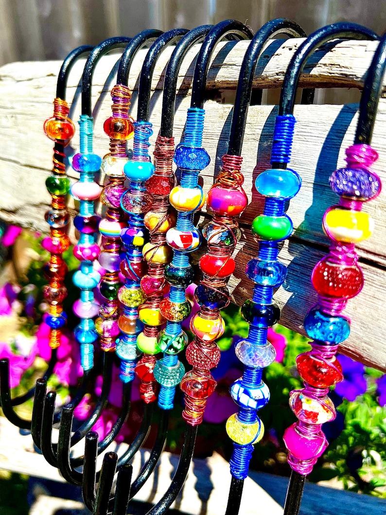 May include: A set of 10 colorful beaded hooks, each with a different pattern of beads. The hooks are made of black metal and are designed to hang on a wall or door. The beads are made of glass and are in various colors, including red, blue, green, yellow, and purple.