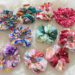 Könnte beinhalten: Sortiment an bunten Stoff-Haargummis mit Blumenmustern. Die Haargummis sind aus weichem, dehnbarem Stoff und perfekt, um das Haar zu fixieren.