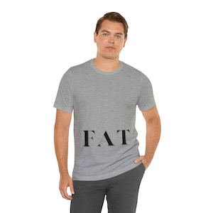 Könnte beinhalten: Ein hellgraues T-Shirt mit dem Wort "FAT" in Schwarz auf der Vorderseite.