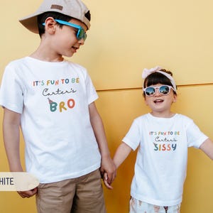 May include: Two children in white t-shirts with the text "IT'S FUN TO BE Carter's BRO" and "IT'S FUN TO BE Carter's SISSY" in colourful letters. The boy wears a cap and sunglasses, and the girl wears sunglasses and a headband.