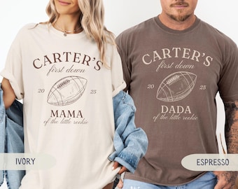 May include: Ivory and espresso-colored t-shirts with the text "CARTER'S first down" and a football graphic. The ivory shirt says "MAMA of the little rookie," and the espresso shirt says "DADA of the little rookie."