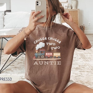 May include: Espresso-colored t-shirt with a train graphic and the text "Chugga Chugga Two Two Auntie". The train is blue, red, and yellow. The shirt is a comfortable, casual style.
