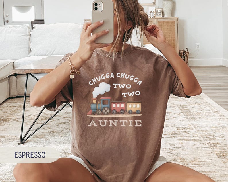May include: Espresso-colored t-shirt with a train graphic and the text "Chugga Chugga Two Two Auntie". The train is blue, red, and yellow. The shirt is a comfortable, casual style.