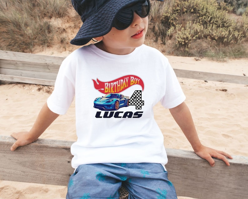 Racing Car Birthday Boy Shirt featuring a red and yellow banner that says Birthday Boy, blue race car, custom name, and custom age in black and white checkered print