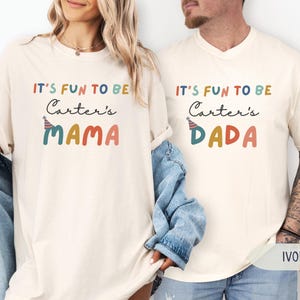 May include: Ivory-coloured t-shirts with the text "IT'S FUN TO BE Carter's MAMA" and "IT'S FUN TO BE Carter's DADA" in colourful lettering. The shirts have a relaxed fit and short sleeves. The word "IVORY" is printed at the bottom.