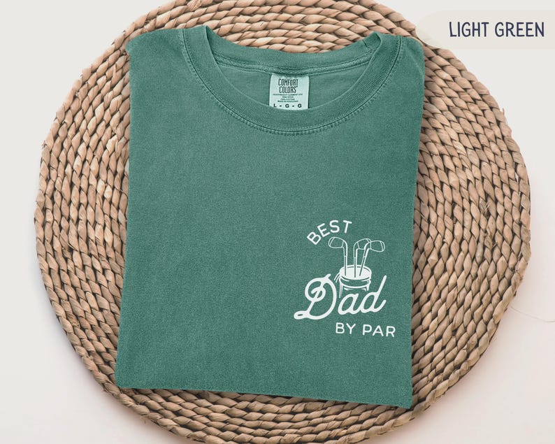 May include: Light green t-shirt with the text "Best Dad By Par" in white. The text is accompanied by a graphic of a golf bag with golf clubs.