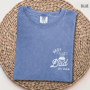 May include: A blue jean t-shirt with white text that says "Best Dad By Par" and a graphic of a golf bag with clubs.
