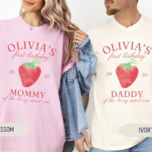May include: Two t-shirts, one blossom pink and one ivory, feature the text "Olivia's first birthday" above a watercolor strawberry. The pink shirt says "Mommy of the berry sweet one," and the ivory shirt says "Daddy of the berry sweet one."