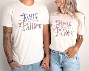 May include: Two cream-colored t-shirts with the text "Dada of the little Fairy" and "Mama of the little Fairy" in purple and gray. The shirts feature butterfly and fairy graphics, perfect for a family.