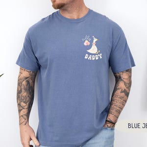Pu&ograve; includere: T-shirt in jeans blu con un'oca di cartone animato che indossa un cappello da festa e tiene dei palloncini. Il testo "Silly Daddy" &egrave; stampato sulla maglietta.