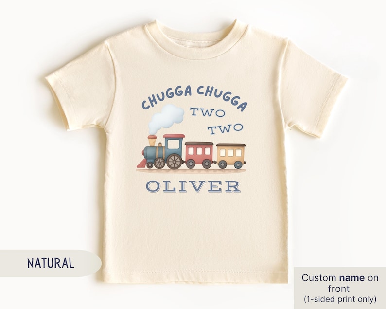 May include: A cream-colored toddler t-shirt with a train graphic. The design includes the text "CHUGGA CHUGGA TWO TWO" above a train illustration and the name "OLIVER" below. The shirt is made of soft material.