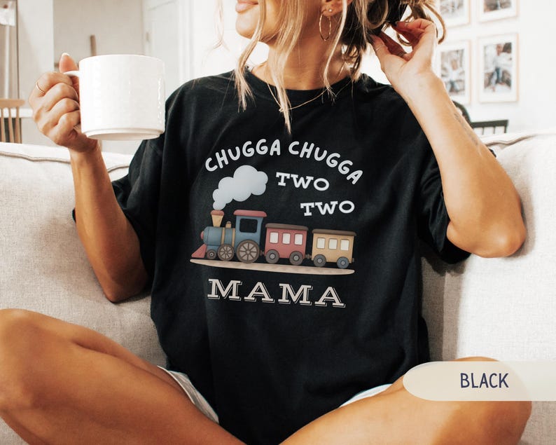May include: Black t-shirt with a colorful train graphic. The design includes the words "CHUGGA CHUGGA TWO TWO TWO MAMA" in white. The train features blue, pink, and brown cars with a white cloud and smoke detail.