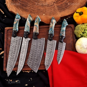 May include: A set of six kitchen knives with patterned blades and colorful, marbled handles. The blades have a textured, damascus steel appearance. The handles feature shades of blue, green, and brown. The knives are arranged on a wooden cutting board.