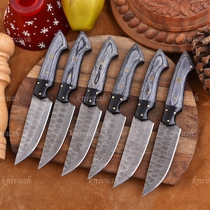 May include: Set of seven kitchen knives with gray and black wooden handles and patterned blades. The handles have brass rivets and black bolsters. The knives are arranged on a wooden cutting board.