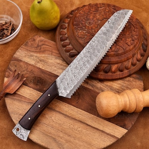 May include: A close-up of a bread knife with a wooden handle and a serrated blade. The blade is made of Damascus steel and has a wavy pattern. The knife is lying on a wooden cutting board.