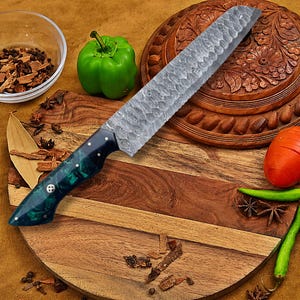 May include: A kitchen knife with a hammered metal blade and a dark green marbled resin handle secured with three silver rivets. The blade features a textured finish, and the handle has a curved ergonomic shape for a comfortable grip during use.