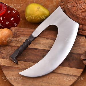 May include: A large, curved, silver-colored cleaver with a twisted black handle. The blade has a unique shape with a cutout near the handle. The cleaver rests on a wooden cutting board, with a pear and other decorative items.